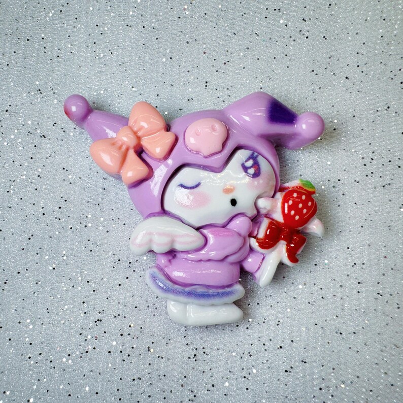 Peut inclure: Un personnage violet et blanc avec un n&oelig;ud rose et une sucette &agrave; la fraise rouge et verte. Le personnage a un &oelig;il qui cligne et un nez rose.