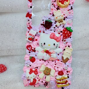 Peut inclure: Une coque de t&eacute;l&eacute;phone rose et blanche d&eacute;cor&eacute;e de Hello Kitty, de fraises et d'autres personnages mignons. La coque est recouverte de gla&ccedil;age rose et blanc et de p&eacute;pites.