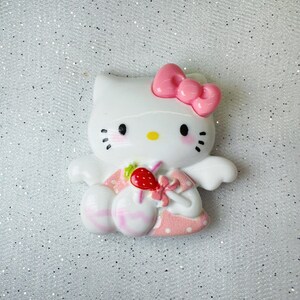Peut inclure: Figurines en c&eacute;ramique blanche de Hello Kitty avec un n&oelig;ud rose, des ailes et une robe. Elle tient une sucette rose et blanche avec une fraise rouge sur le dessus.