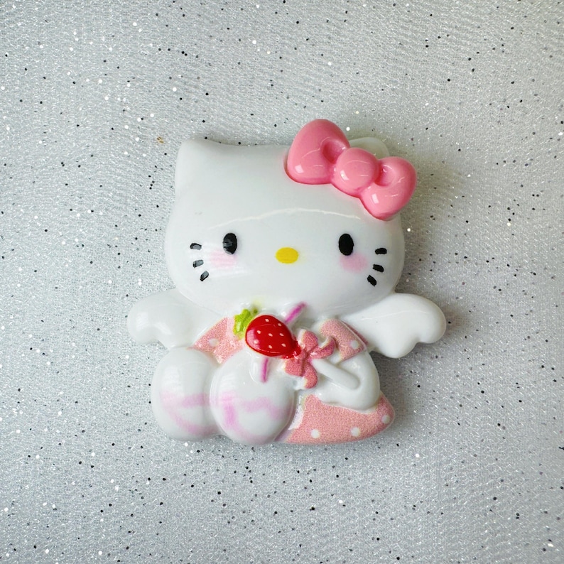 Peut inclure: Figurines en c&eacute;ramique blanche de Hello Kitty avec un n&oelig;ud rose, des ailes et une robe. Elle tient une sucette rose et blanche avec une fraise rouge sur le dessus.