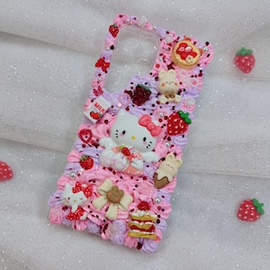 Peut inclure: Une coque de t&eacute;l&eacute;phone rose et violette d&eacute;cor&eacute;e de Hello Kitty, de fraises et d'autres d&eacute;tails mignons. La coque a un dos transparent pour montrer le t&eacute;l&eacute;phone.