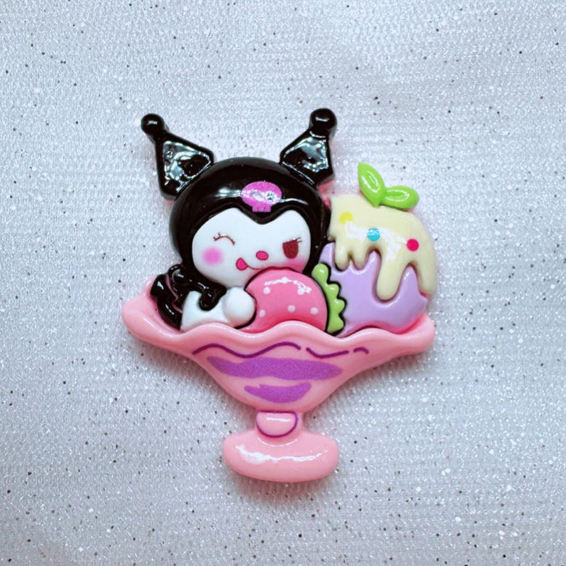 May include: A pink and purple ice cream sundae charm featuring a black and white cartoon character with a pink strawberry and a purple and yellow ice cream scoop.