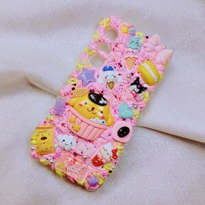 May include: A pink phone case decorated with colorful 3D embellishments, including a yellow cartoon character, a pink cupcake, a blue ice cream cone, and a pink and white bow. The case is covered in glitter and has a pink and white swirl design.