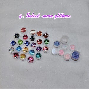 May include: An assortment of small, clear plastic containers filled with colorful glitter. The glitter colors include red, green, blue, gold, and pink. The text "4. Select some glitters" is written in purple script.