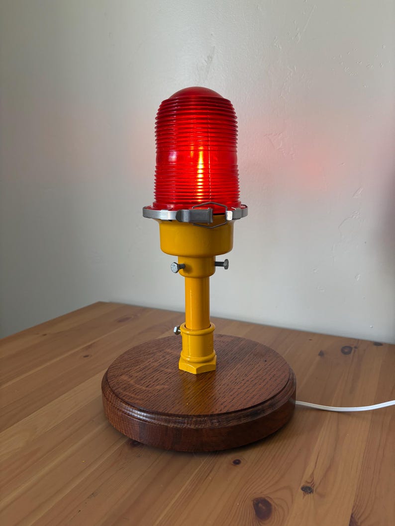 May include: A yellow and red industrial style lamp with a red lens and a wooden base.