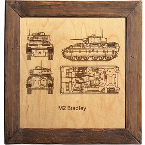 May include: Wooden framed artwork featuring detailed blueprints of an M2 Bradley tank. The artwork includes front, side, and top views, along with the text "M2 Bradley" etched into the wood. The frame is a dark brown color.
