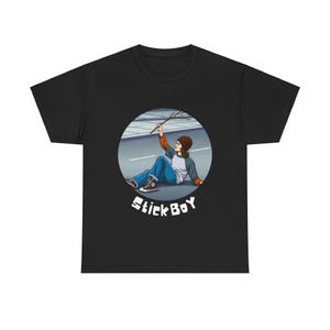 May include: Black t-shirt featuring a circular graphic of a person sitting on pavement, holding a stick. The person is wearing a brown beanie, blue jeans, and a gray and white long-sleeve shirt. The text "Stick Boy" is below the graphic.