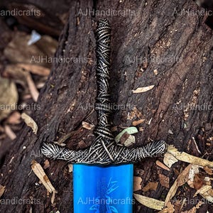 May include: A blue and silver sword with a detailed hilt. The sword is lying on a bed of brown leaves and bark.