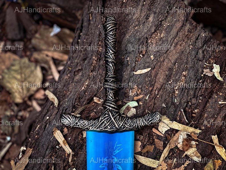 May include: A blue and silver sword with a detailed hilt. The sword is lying on a bed of brown leaves and bark.