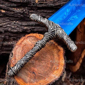 May include: A blue and silver sword with a detailed hilt and a blue blade. The sword is resting on a wooden surface.
