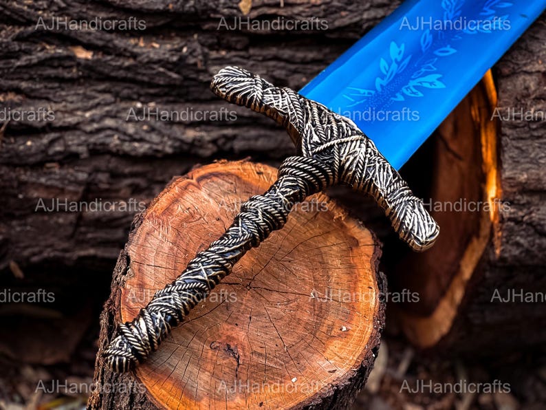May include: A blue and silver sword with a detailed hilt and a blue blade. The sword is resting on a wooden surface.