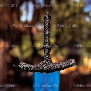 May include: A close-up of a sword with a black, braided handle and a blue blade. The blade has a decorative design etched into it.