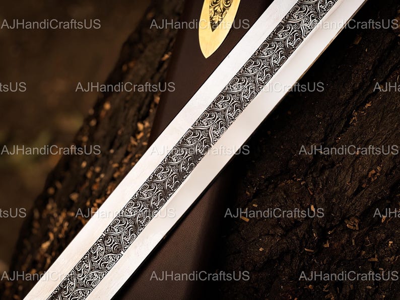 May include: Close-up of a sword blade with a detailed, ornate design running down the center. The blade is silver, and the central design is black and silver. The text "AJHandiCraftsUS" is visible in the image.