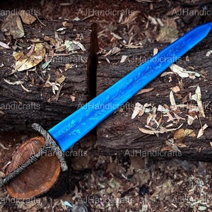 May include: A blue sword with a floral design on the blade. The sword is lying on a wooden log with brown bark and is surrounded by fallen leaves.