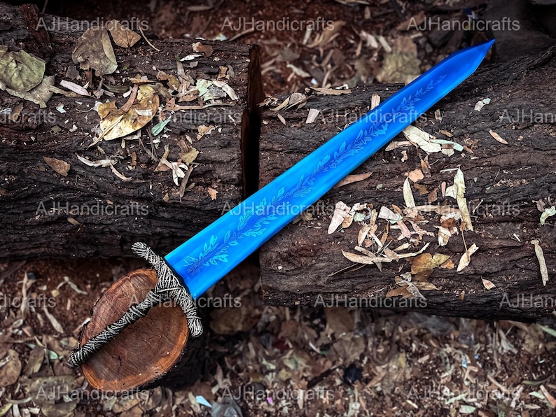 May include: A blue sword with a floral design on the blade. The sword is lying on a wooden log with brown bark and is surrounded by fallen leaves.
