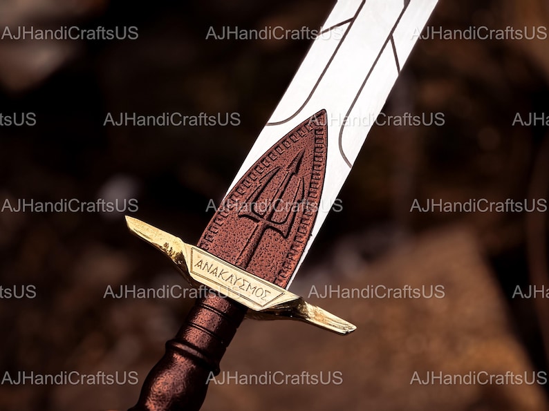 May include: A close-up of a decorative sword with a bronze handle and a silver blade. The sword features a bronze guard with the Greek word "ANAKLYSMOS" and a trident symbol. The blade is white with etched lines.