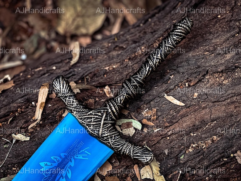 May include: A blue and silver sword with a detailed design on the hilt. The sword is lying on a piece of wood with brown bark.