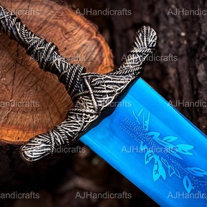 May include: A blue sword with a silver handle and a decorative design. The sword is lying on a wooden surface.