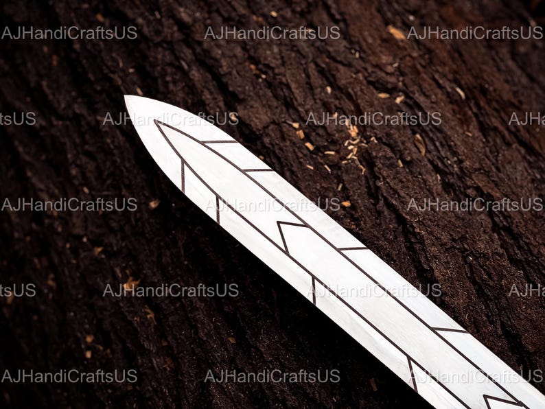 May include: A decorative, white sword blade with black geometric designs. The blade is set against a dark brown, textured wooden surface. The text "AJHandiCraftsUS" is visible in the background.