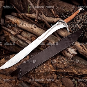 May include: A curved sword with a silver blade and a brown leather-wrapped handle. The sword is accompanied by a dark brown leather sheath. The blade has decorative etchings. The sword and sheath are displayed on a bed of wooden logs.