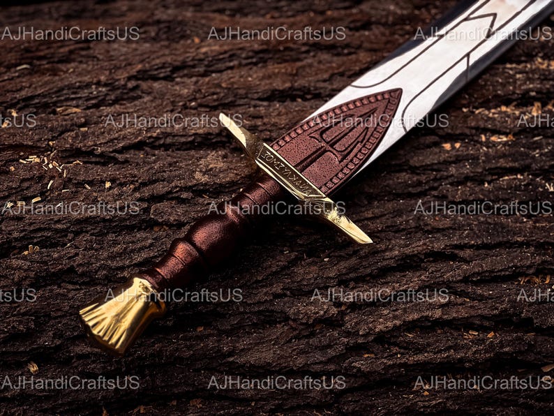 May include: A close-up of a decorative sword with a brown handle and a gold-colored hilt. The blade is silver with a brown emblem. The sword rests on a textured, dark brown surface.