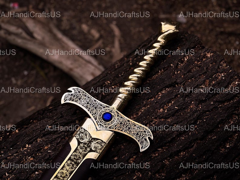 May include: A decorative sword with a gold-colored hilt and blade, featuring intricate engraved patterns and a blue gem. The sword rests on a dark, textured wooden surface, showcasing its ornate design.