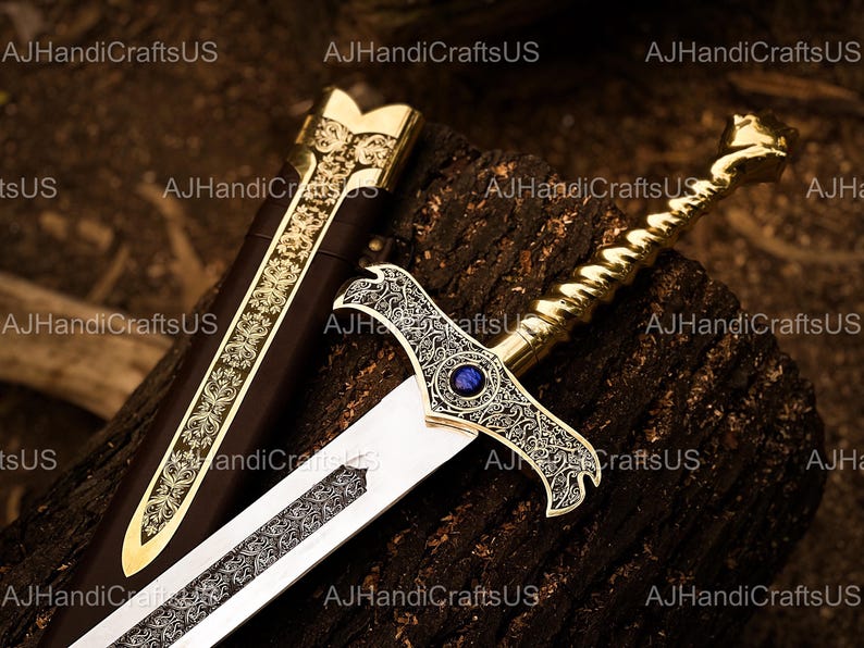 May include: An ornate sword with a gold handle and a silver blade rests on a wooden surface. The hilt features intricate designs and a blue gem. The scabbard is brown with gold accents. The sword is a decorative item.