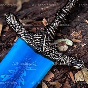 May include: A blue and silver sword with a detailed design on the hilt. The sword is lying on a bed of brown leaves.