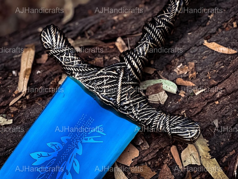 May include: A blue and silver sword with a detailed design on the hilt. The sword is lying on a bed of brown leaves.