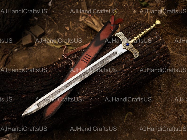 May include: A decorative sword with a silver blade and ornate gold hilt, featuring a blue gem. The sword rests on a dark wooden surface next to a red leather sheath. The blade has a detailed etched design.