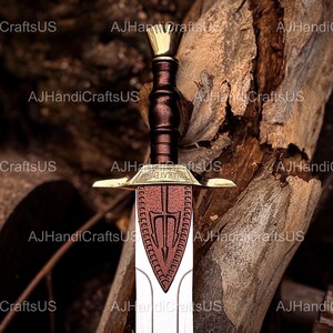 May include: A decorative sword with a gold-colored hilt and crossguard, a brown leather-wrapped handle, and a red and white blade. The sword features a crown-shaped pommel and is set against a wood background.