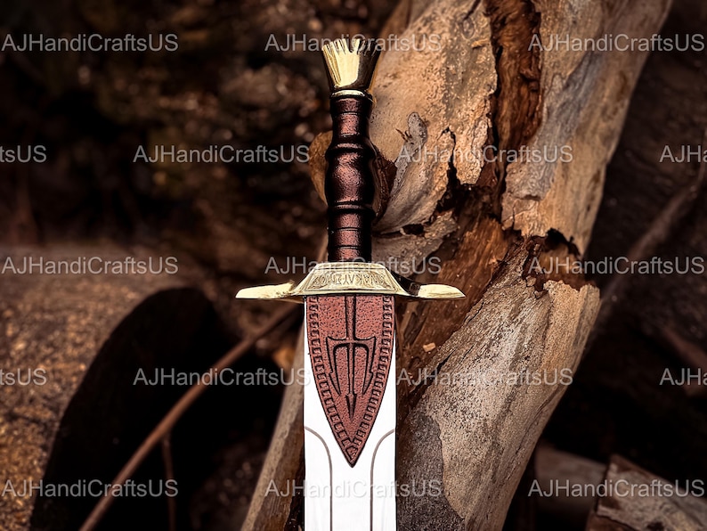 May include: A decorative sword with a gold-colored hilt and crossguard, a brown leather-wrapped handle, and a red and white blade. The sword features a crown-shaped pommel and is set against a wood background.