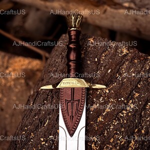 May include: A detailed image of a sword with a brown handle and a gold-colored hilt. The blade is silver with a brown emblem. The sword rests on a textured, dark brown surface. The text "&Psi;&Eta;&Nu;&Kappa;&Nu;&Alpha;&Sigma;&Kappa;&Omicron;" is visible on the hilt.