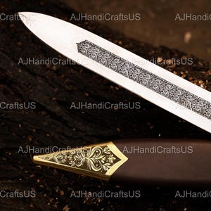 May include: A detailed image of a sword with a silver blade and ornate engravings. The hilt is encased in a brown sheath with a gold-colored, decorative tip. The text "AJHandiCraftsUS" is visible in the image.