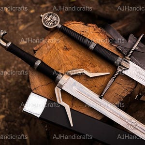 May include: Two decorative swords with black handles and silver blades rest on a wooden surface. One sword has a circular pommel, while the other features a stylized dragon head. The blades are engraved with text.