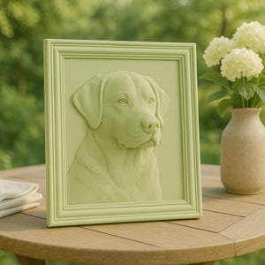 Könnte beinhalten: Gerahmte, hellgrüne Flachreliefskulptur eines Labrador Retriever-Hundes. Kopf und Schultern des Hundes sind detailliert in einem rechteckigen Rahmen dargestellt. Rahmen und Skulptur haben eine passende hellgrüne Farbe. Die Skulptur wird auf einem Holztisch ausgestellt.