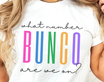Puede incluir: Camiseta blanca con la frase "what number BUNGO are we on?" en letras coloridas. La palabra "BUNGO" es rosa, azul, verde, naranja y morado. Una camiseta de estilo casual.
