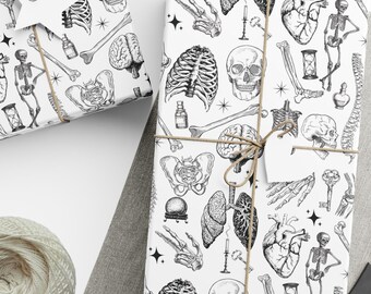 May include: White wrapping paper with a black anatomical illustration pattern, tied with twine. The image includes wrapped gifts, a ball of twine, scissors, and blank tags. The pattern features human anatomy elements like skulls, hearts, and bones.