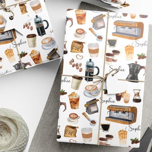 May include: White wrapping paper with a coffee-themed pattern featuring coffee cups, espresso machines, and coffee beans. The paper is tied with twine and a tag that says "Sophie". A ball of twine, scissors, and blank tags are also visible.