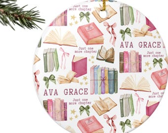 Peut inclure: Une décoration de Noël ronde blanche avec une ficelle dorée. Elle est ornée d'illustrations à l'aquarelle de livres, de nœuds et d'étoiles. Le nom "AVA GRACE" et la phrase "Just one more chapter" sont imprimés.