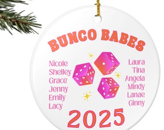 May include: A white, round Christmas ornament with the text "BUNCO BABES" in orange. The ornament features pink dice graphics and the year 2025. Names of the group members are listed in pink. A gold string is attached for hanging.