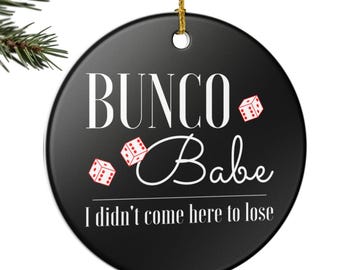 May include: A black round ornament with the words "Bunco Babe" in white script and the phrase "I didn't come here to lose" in white. Red dice graphics are scattered around the text. The ornament hangs from a gold string.