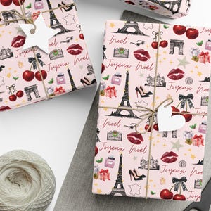 May include: Light pink wrapping paper featuring a repeating pattern of black Eiffel Towers, red cherries, high heels, lipstick kisses, perfume bottles, and the text Joyeux Noel in cursive script, tied with twine and white star or heart gift tags.