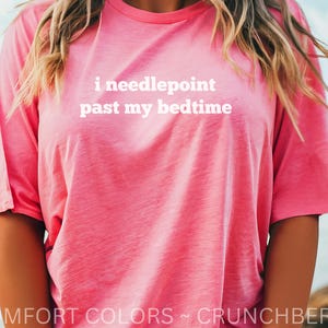 May include: A pink t-shirt with the text "i needlepoint past my bedtime" in white. The shirt is a Comfort Colors brand in the color Crunchberry. The short-sleeved shirt is a solid color and is worn by a person.