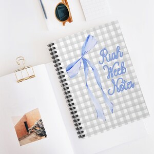 Op de afbeelding: Een grijs en wit geruit notitieboek met een blauwe strik en de tekst "Rush Week Notes".