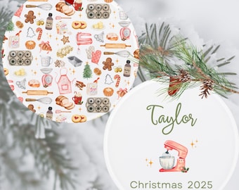 May include: Two white Christmas baubles. One has a pattern of baking illustrations including gingerbread men, rolling pins, and mixers. The other bauble has the name "Taylor" in green script, a pink mixer, and the text "Christmas 2025".