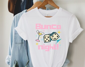 May include: White t-shirt with a pink graphic that says "Bunco night!" with a martini glass and two dice.