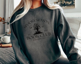 Puede incluir: Una sudadera gris oscura con un estampado gráfico negro que dice "Spooky Season Book Club Est. 2024 Invitation Only" con un árbol espeluznante y murciélagos.
