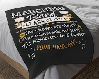 Può includere: Coperta in pile nera con testo bianco che recita "Marching Band Class of 2024". Il testo continua con "The shows are short, the rehearsals are long, the memories last forever". Il testo "YOUR NAME HERE" è in giallo.