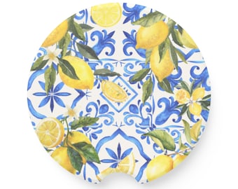 May include: A round car coaster featuring a watercolor design of lemons and leaves on a white and blue tile pattern. The coaster has a cutout for easy removal and placement in a car cup holder.
